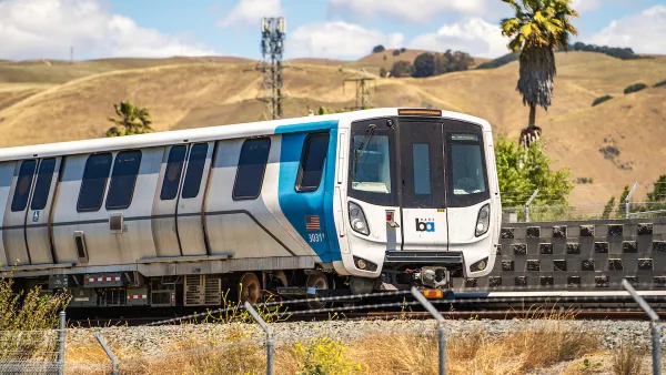 A white and blue Bay Area Rapid Transit (BART) train with golden hills and a palm tree in background.