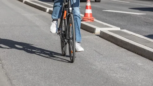 Close-up of person on road bike riding on protected bike lane separated by concrete curb from street.