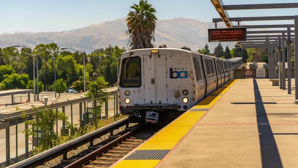 San Francisco Bay Area Rapid Transit train at elevated station with hills and palm tree in background.