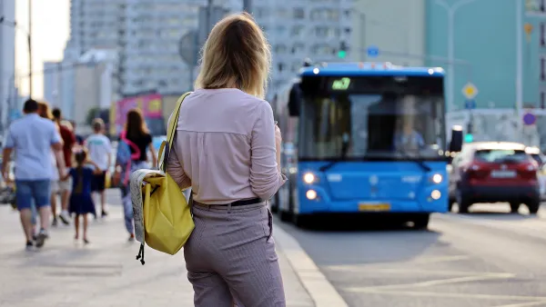 Woman waiting at city bus stop with blue bus pulling up.