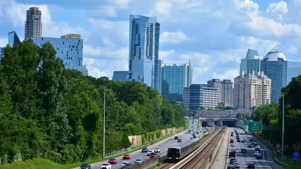 MARTA train tracks run in the middle of a six lane highway with an overpass and the Buckhead city skyline of skyscrapers in the background.