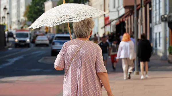Older woman walking on city street holding white lace sun parasol.