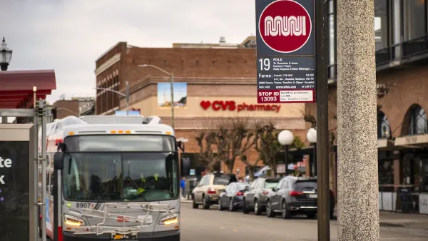 Close-up of white and red Muni sign at bus stop on Polk Street in San Francisco, California with blurred bus in background.