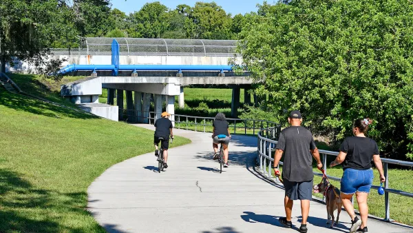 Concrete bike and pedestrian trail with people walking and biking under pedestrian bridge in Orlando, Florida.