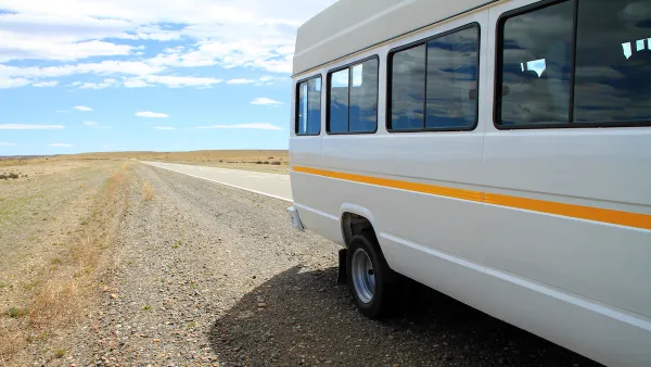 White microbus with yellow stripe on rural road with empty road and blue sky in background.