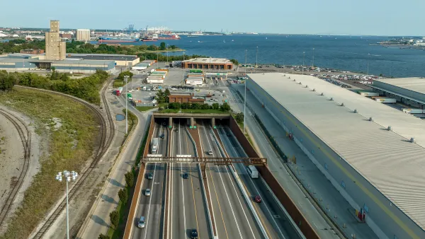 Aerial view of an eight-lane highway tunnel with the harbor in the background.