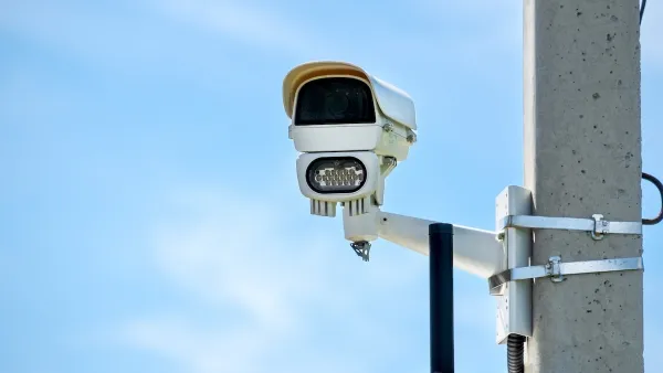 Close-up of white traffic enforcement camera mounted on concrete pole against blue sky.