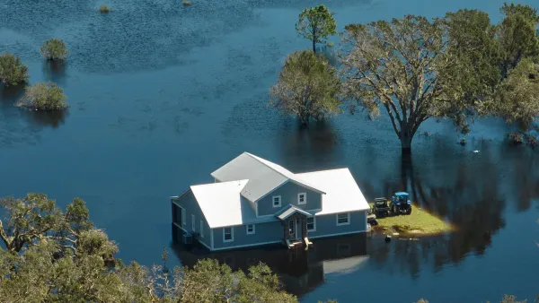 A gray hope with white roof surrounded by floodwaters that come up just above the home's foundations.