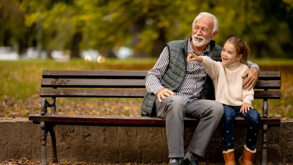 Grandfather and young girl sitting on park bench.
