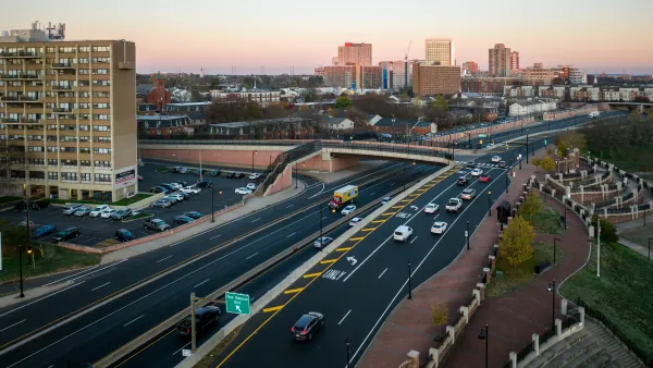 Overhead view of highway with offramps leading to overpass and buildings in the distance.