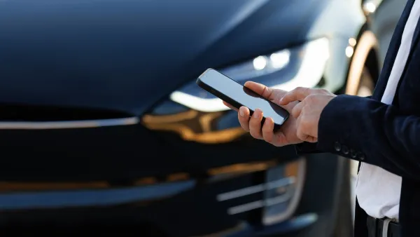 Close-up of hand holding smartphone and Tesla car hood in background.