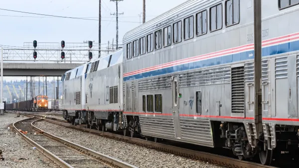 Silver and blue Amtrak train approaching an oncoming orange freight train at station in Seattle, Washington.
