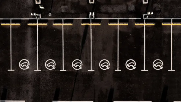 Overhead view of black asphalt parking lot with white lined parking spots with EV charging logos.