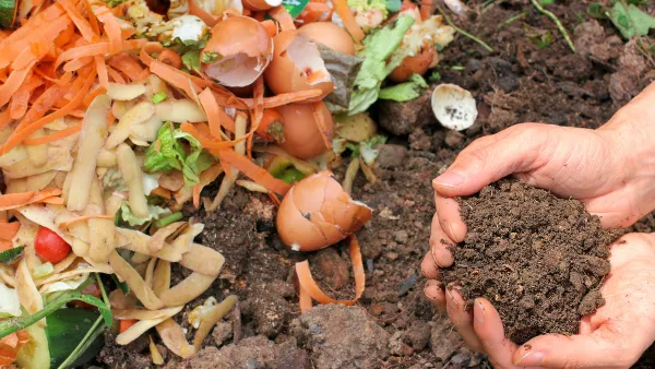Pair of hands holding compost above pile of soil and food scraps.