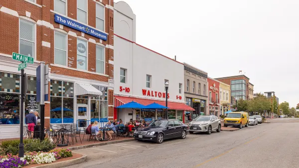 Main Street in Bentonville, Arkansas with three-story brick buildings, people sitting at tables on sidewalk, and sign on building for "The Walmart Museum."