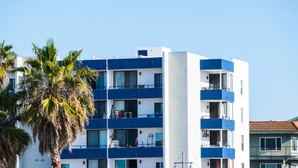 Top floors of blue and white apartment building with palm trees against sunny blue sky in Malibu, California.