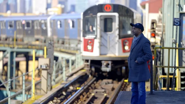 Subway train pulling into elevated outdoor platform in New York City with one passenger waiting.
