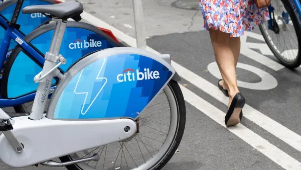 Close-up of Citi Bike electric bikes at on-street station in New York City next to bike lane with woman walking a bike.