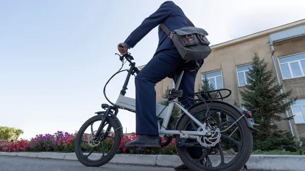 Person on folding electric bike wearing messenger bag resting foot on ground on urban street.