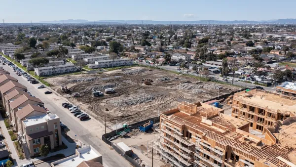 Aerial view of large construction site and vacant, graded lot next to public housing buildings in Watts, Los Angeles, California.