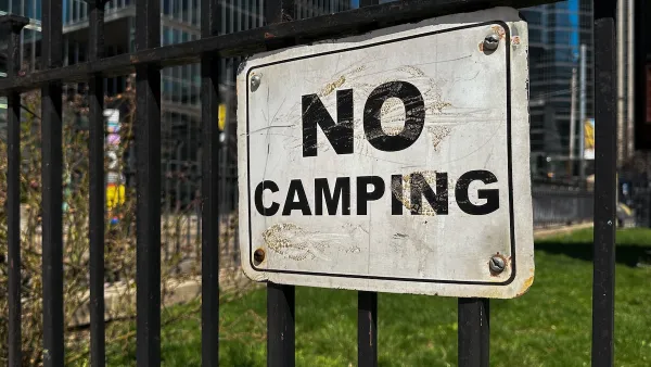 Close-up of white and black NO CAMPING sign on black iron fence.