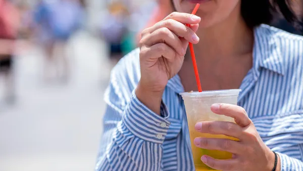 Close-up of woman in blue and white striped button-up shirt drinking from clear plastic cup with red straw.