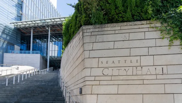 Close-up of engraved stone Seattle City Hall sign in front of wide steps leading to modern glass building.