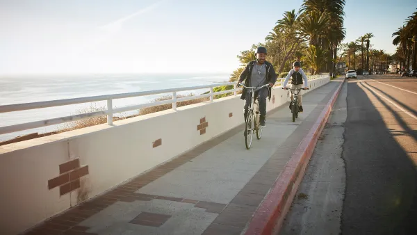 Father and son riding bikes on a sidewalk next to a road withough bike lane on California coast with palm trees in background at golden hour.