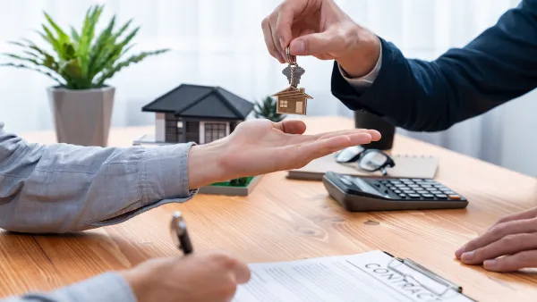 Close-up of person signing home or apartment contract and receiving house key with house-shaped keychain.