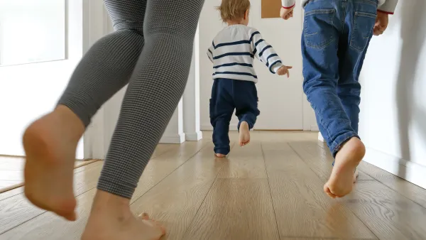 Close-up of two adults running after a small toddler in a bright apartment hallway