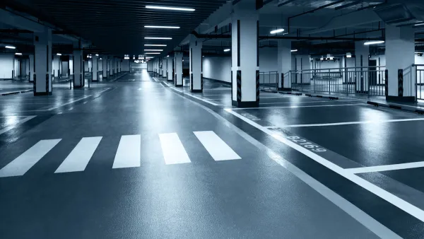 Black and white tinted photo of underground parking garage with black floor, white crosswalk, and harsh lighting.