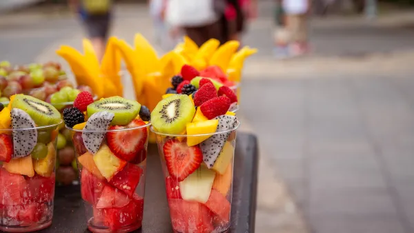 Close-up of rows of clear plastic cups filled with cut fruit on outdoor street vendor table
