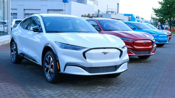 Row of white, red, and blue electric Ford Mustang Mach-E cars at dealership in Frankfurt, Germany.