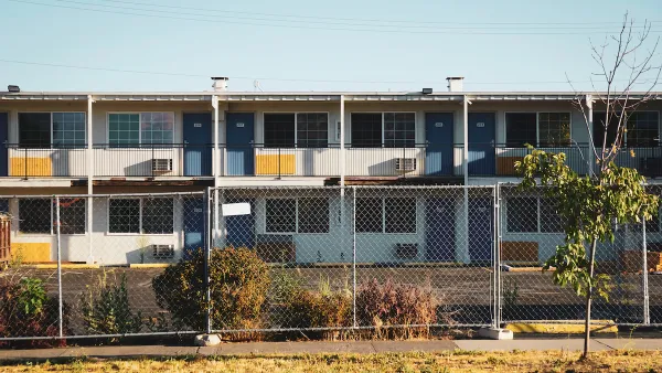 Closed, boarded-up two-story motel behind chain-link fence.