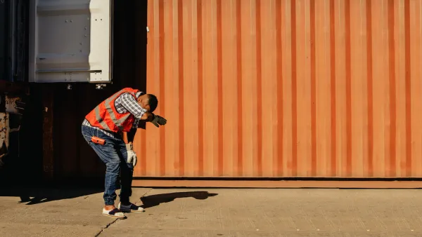 Worker in safety vest leaning over expressing heat exhaustion standing next to orange shipping container.
