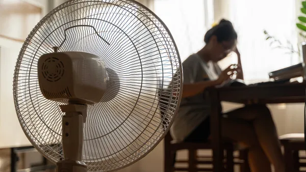 Close-up of floor fan operating with blurred woman sitting at table in background.