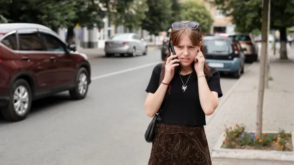 Girl on phone struggling to hear standing on loud city street.