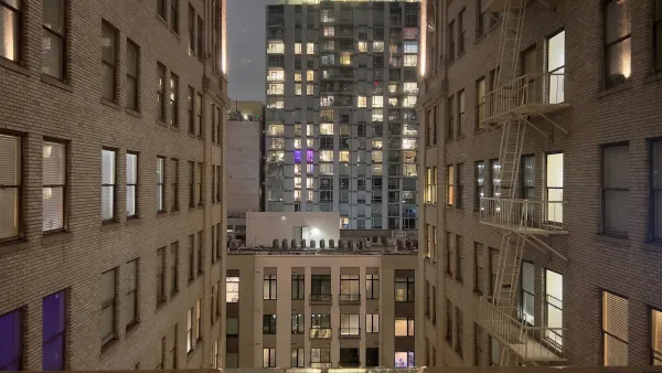 View from between tall white brick buildings in evening in downtown Los Angeles with modern office building across street.