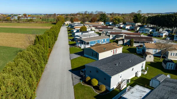 Aerial view of mobile home community in rural area with homes lined up diagonally next to small road.