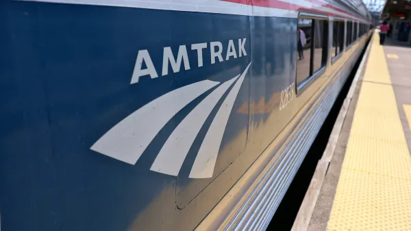 Close-up of Amtrak logo on blue passenger train stopped at outdoor station platform.