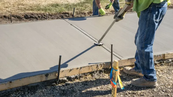Workers pouring concrete in wooden mold for new sidewalk