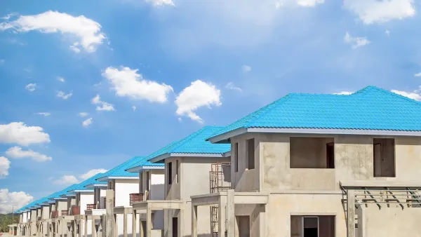 Row of concrete two-story homes with blue tile roofs under construction.