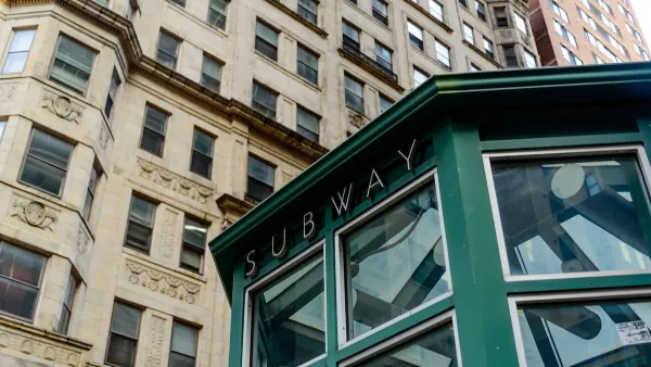 Green subway station entrance kiosk with brick buildings in background.