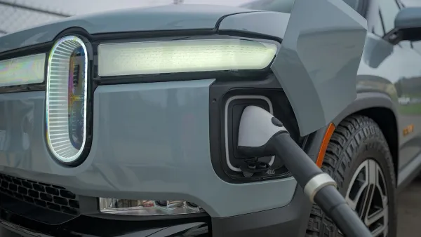 Close-up of front corner of grey Rivian truck with charger plugged in.
