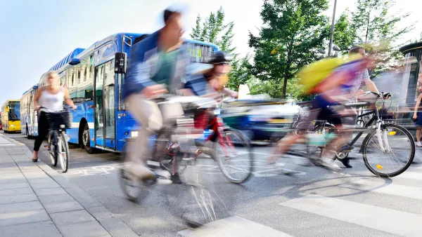 Blurred bicyclists riding through crosswalk with blue bus behind them.