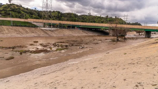 Water flowing through Glendale Narrows section of Los Angeles River in Glendale, California with a concrete bridge, power lines, and hills in background.