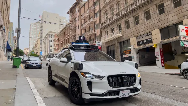 White Waymo self-driving taxi on street in San Francisco, California with brick buildings in background.