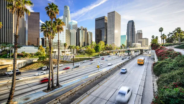View of traffic on freeway with Los Angeles skyline and palm trees in background
