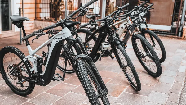 Black e-bikes sitting on a sidewalk outdoors.