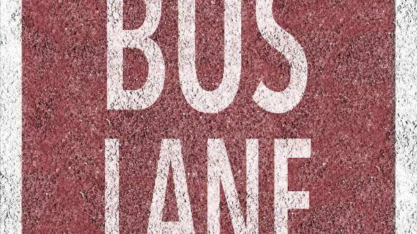 Overhead view of white BUS LANE sign painted on red background on concrete street.